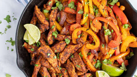 Overhead of a cat iron filled with skillet chicken fajitas and bright colored bell peppers garnished with pieces of cilantro.