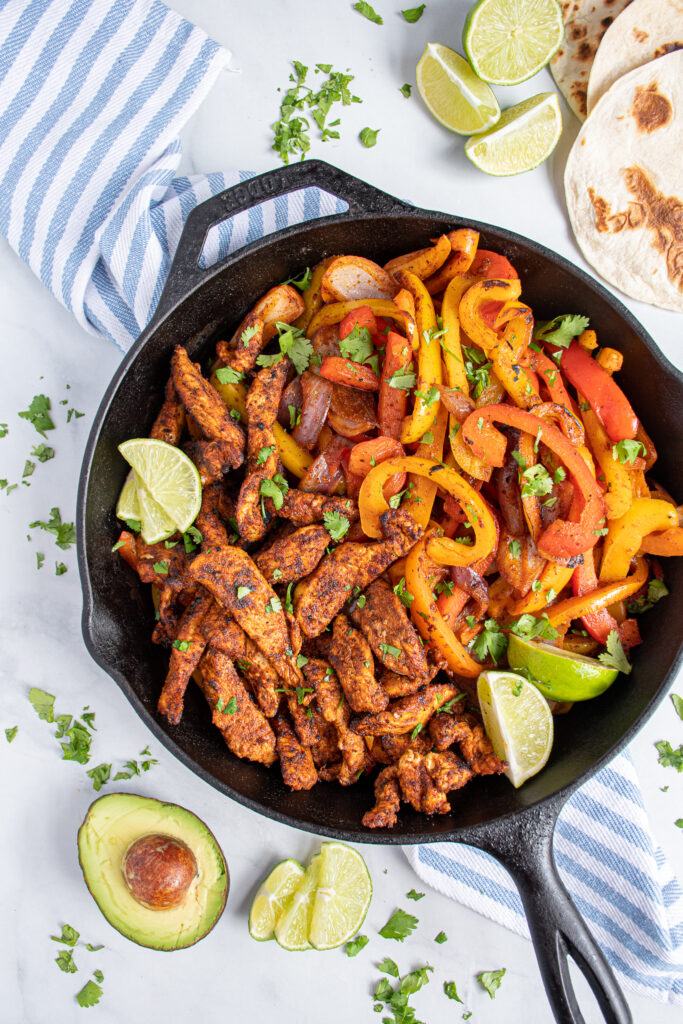 Overhead of a cat iron filled with skillet chicken fajitas and bright colored bell peppers garnished with pieces of cilantro.