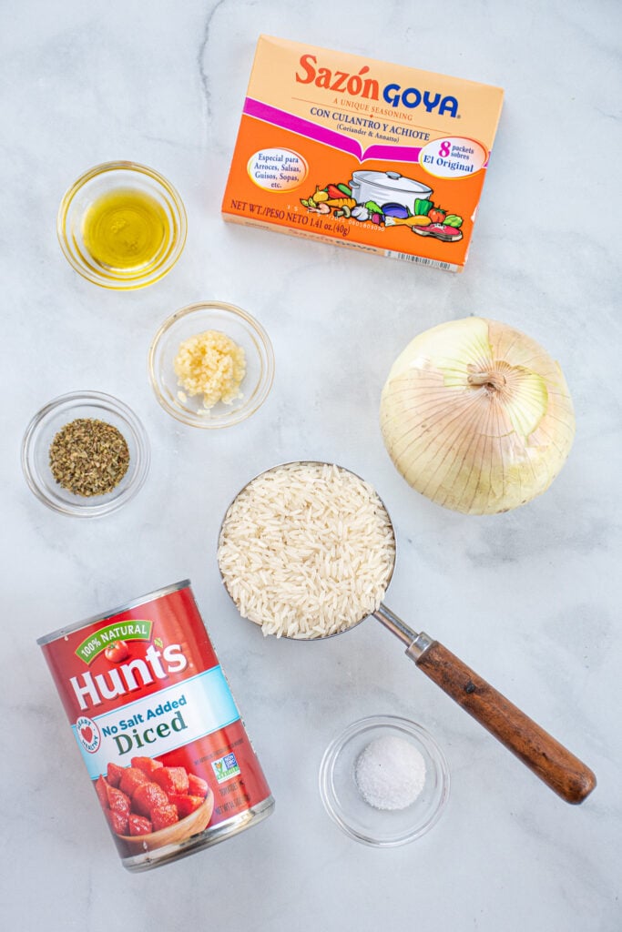 Ingredients needed to make mexican rice arranged on a table top including Sazón Goya Con Cilantro Y Achiote.