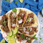 Pinterest Pin with text overlay 'Slow Cooker Beef Barbacoa', image of plate with a bunch of tacos filled with barbacoa and garnished with cilantro.