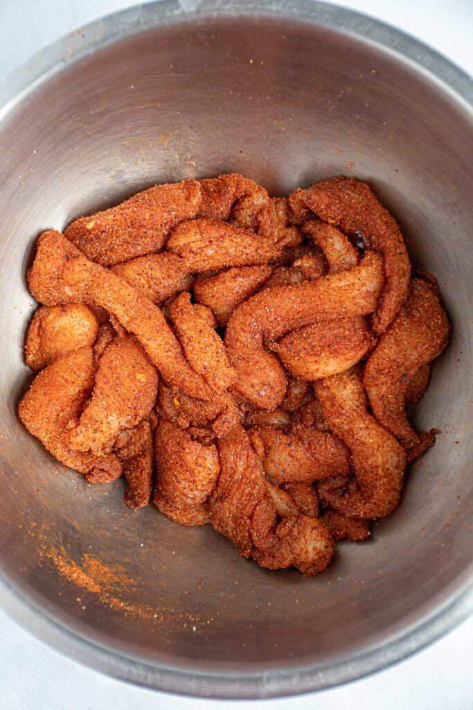 Seasoning chicken with fajita seasoning in a bowl.