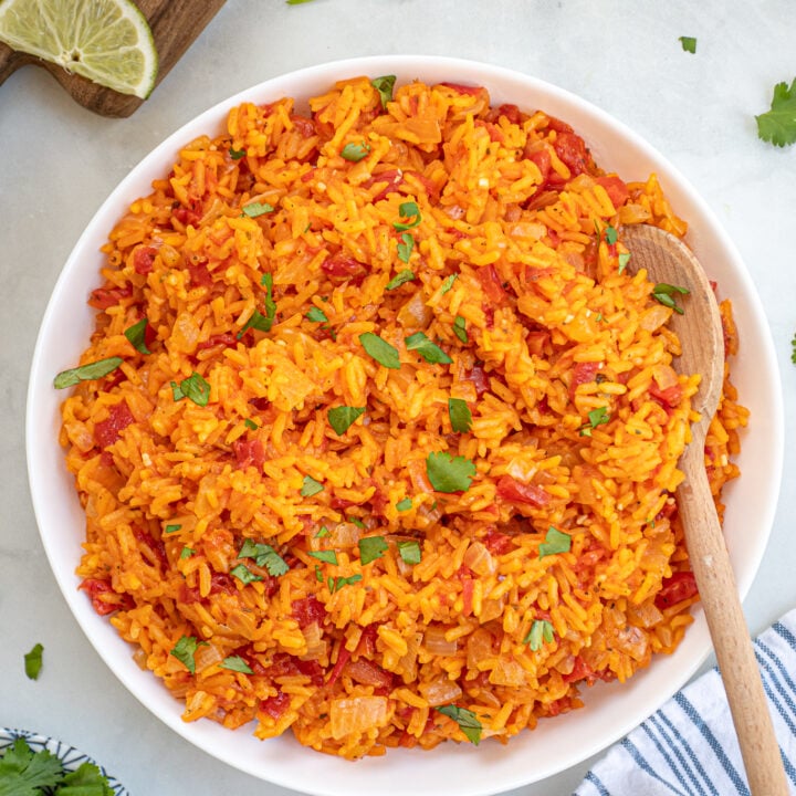 A white bowl with a wooden spoon filled with mexican rice and garnished with cilantro.