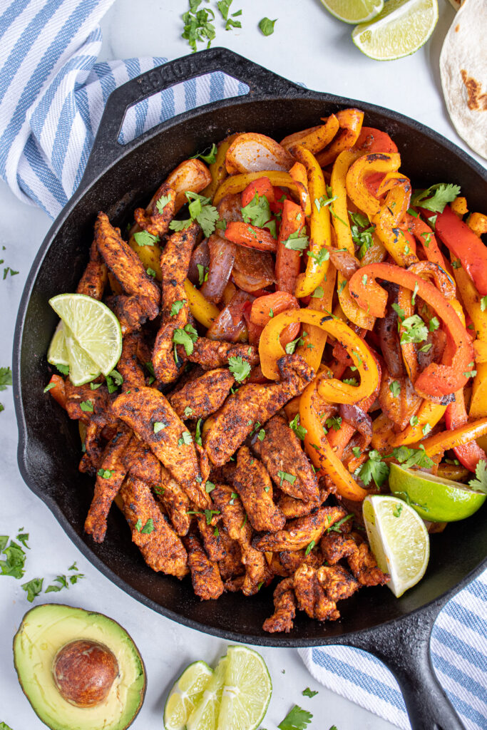 Skillet filled with chicken fajitas and bright bell peppers garnished with pieces of cilantro.