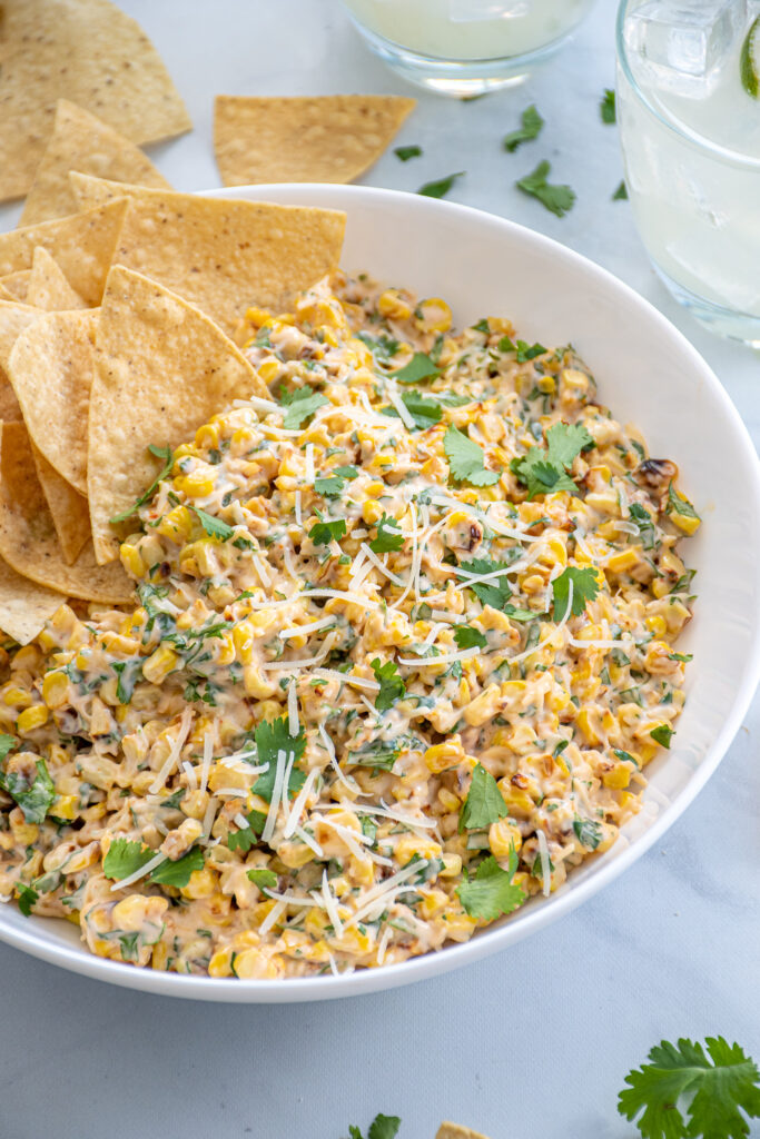 Mexican Street Corn Dip in a bowl garnished with parmesan cheese and cilantro with a handful of tortilla chips on the side.