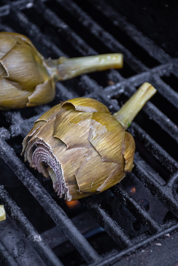 Close up of half an artichoke on a grill grate.