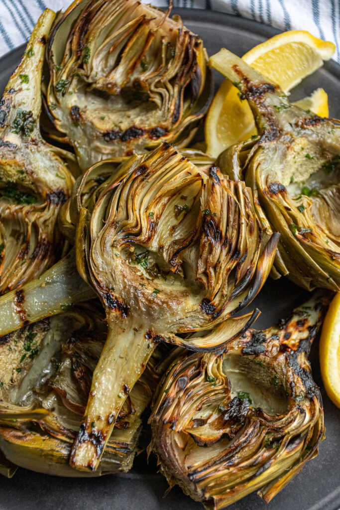 Close up of a platter full of grilled artichokes, close up on a single artichoke with grill marks on it.