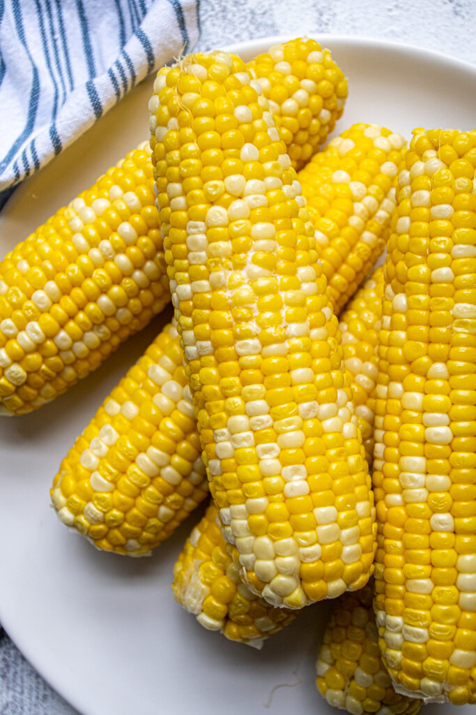 Close up of an ear of corn on a plate, melted butter is in between the bright yellow kernels.