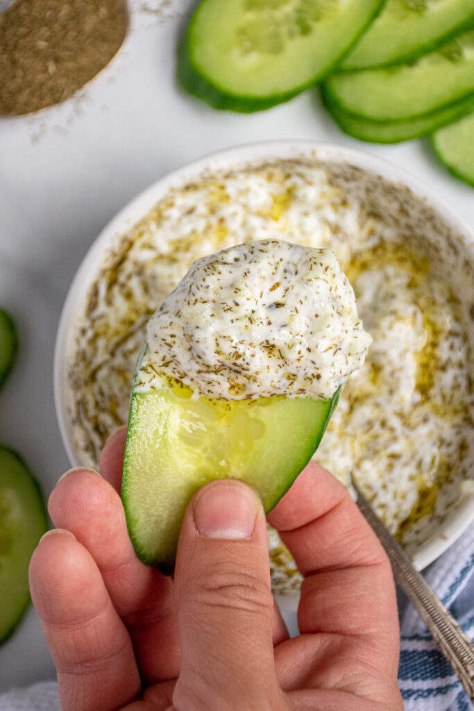 A cucumber slice with a large scoop of tzatziki sauce dipped onto it.