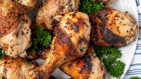 A white plate full of grilled greek marinated chicken drumsticks showing off crispy brown skins.