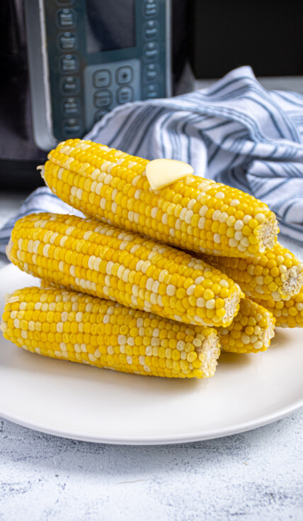 Pyramid shaped stack of freshly cooked instant pot corn on the cob showing off bright yellow kernels complete with a slab of melted butter on top.