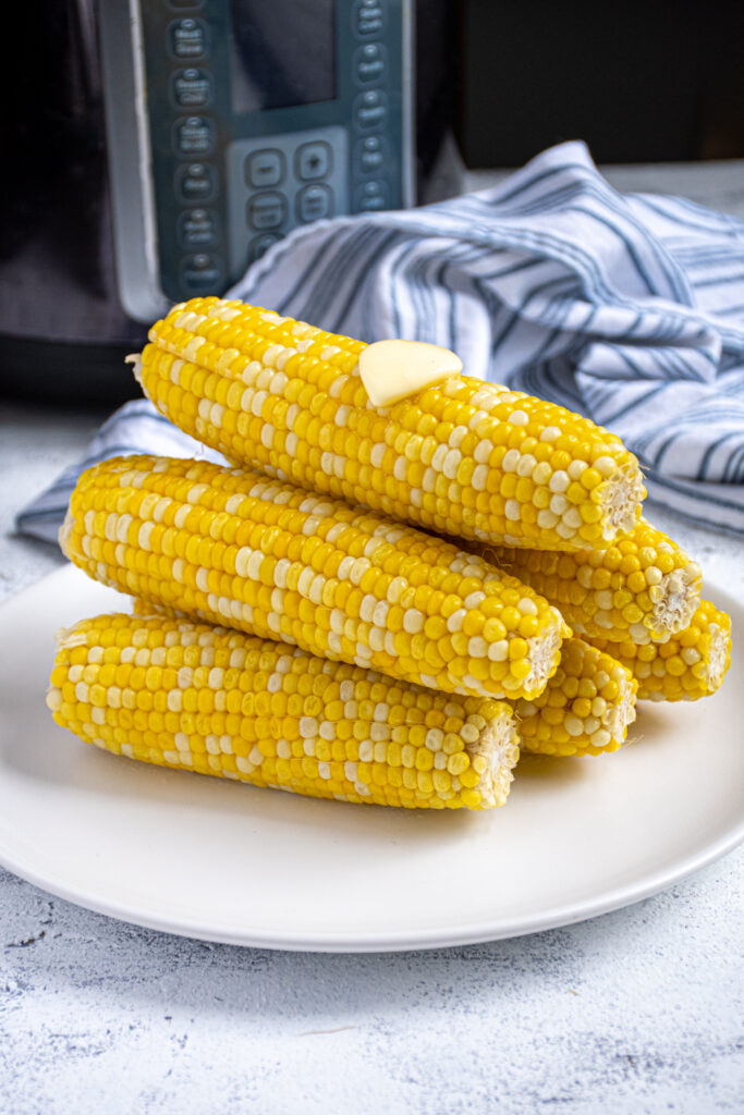 Pyramid shaped stack of freshly cooked instant pot corn on the cob showing off bright yellow kernels complete with a slab of melted butter on top.