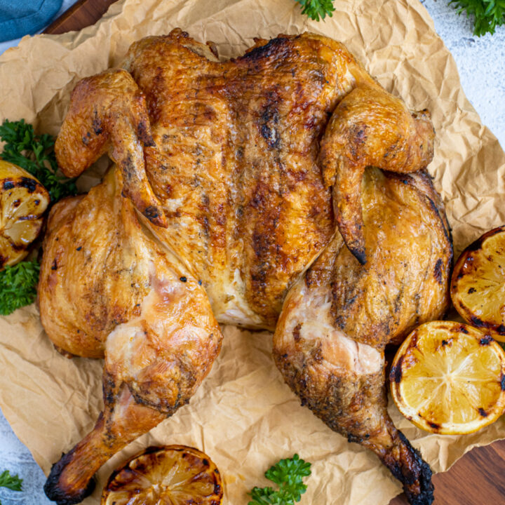 Overhead view of a spatchcocked chicken grilled to golden brown perfection sitting on butcher paper on a cutting board.