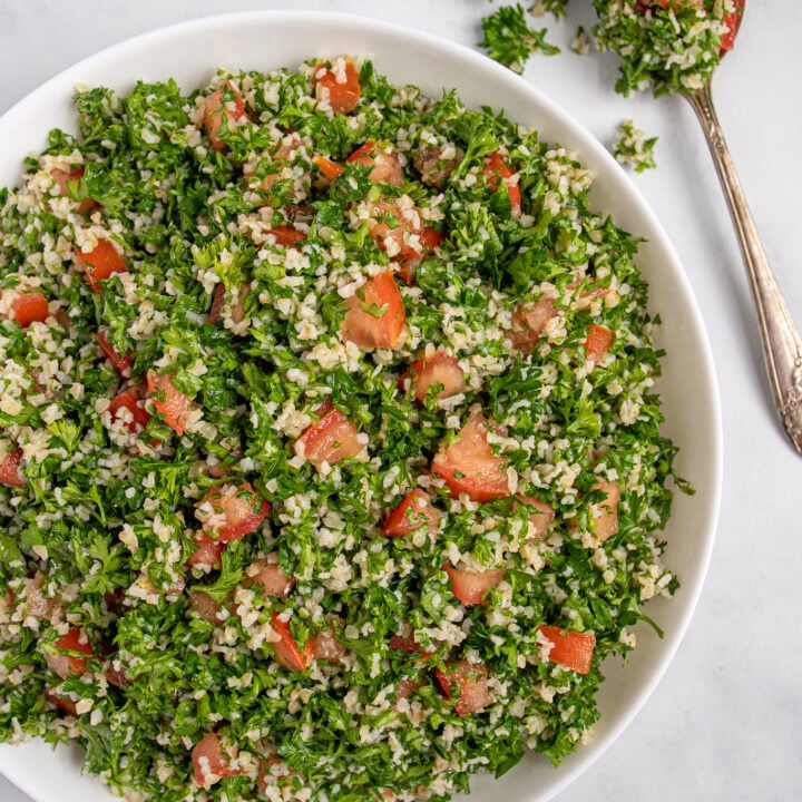 Overhead view of tabbouleh salad in a large white bowl with bright red tomatoes peeking through like jewels.