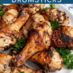 Pinterest Pin with text 'Greek Inspired Grilled Chicken Drumsticks', image of a plate piled high with golden brown grilled chicken legs.