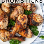 Pinterest Pin with text 'Greek Marinated Grilled Chicken Drumsticks', image of a plate piled high with golden brown grilled chicken legs.