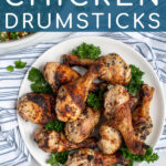 Pinterest Pin with text 'Greek Marinated Chicken Drumsticks', image of a plate piled high with golden brown grilled chicken legs.