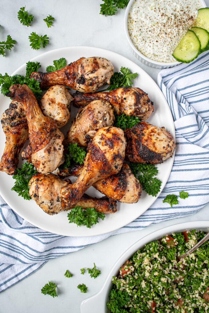 A plate piled high with grilled chicken drumsticks that are golden brown from an easy greek marinade.