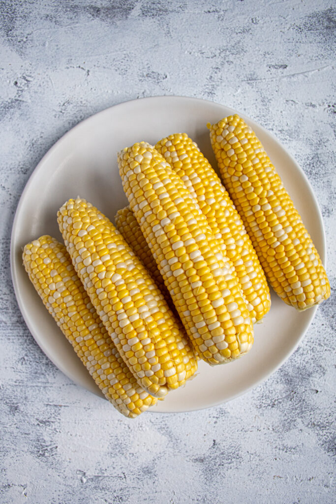 White plate full of a stack of raw sweet corn on the cob.