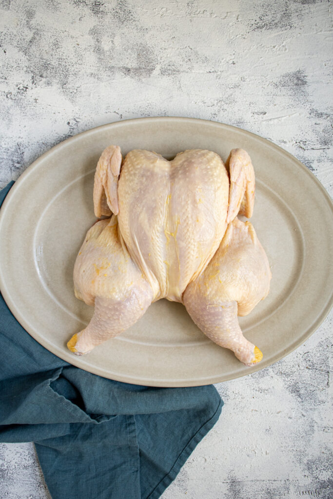 A raw spatchcocked chicken laid out on a white platter.