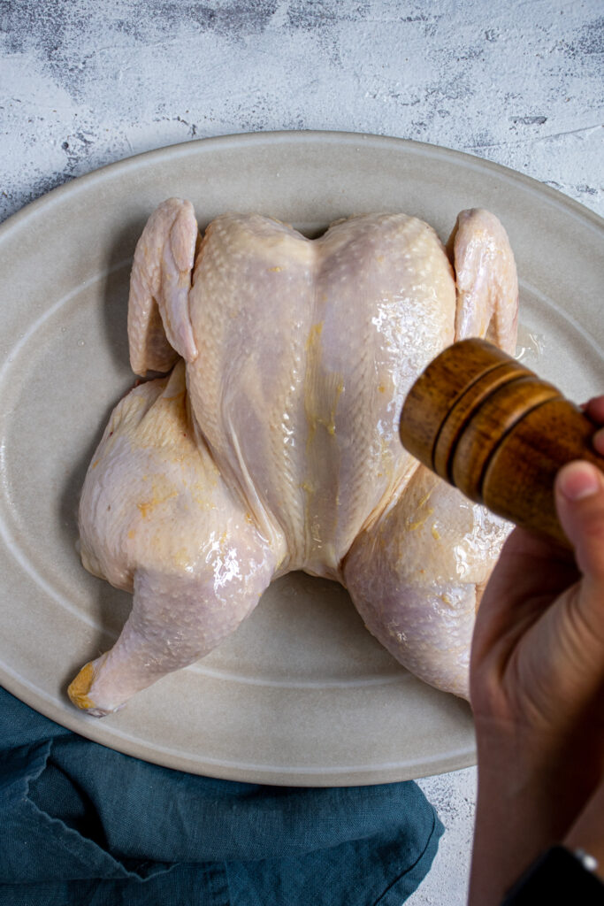 Salting an oiled and spatchcocked chicken getting it ready to grill.
