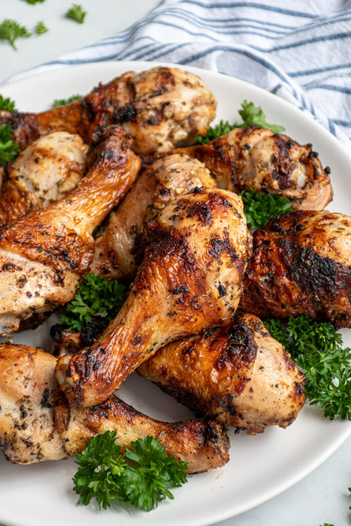 Close up photo of a grilled chicken drumstick on a pile of chicken on a plate.