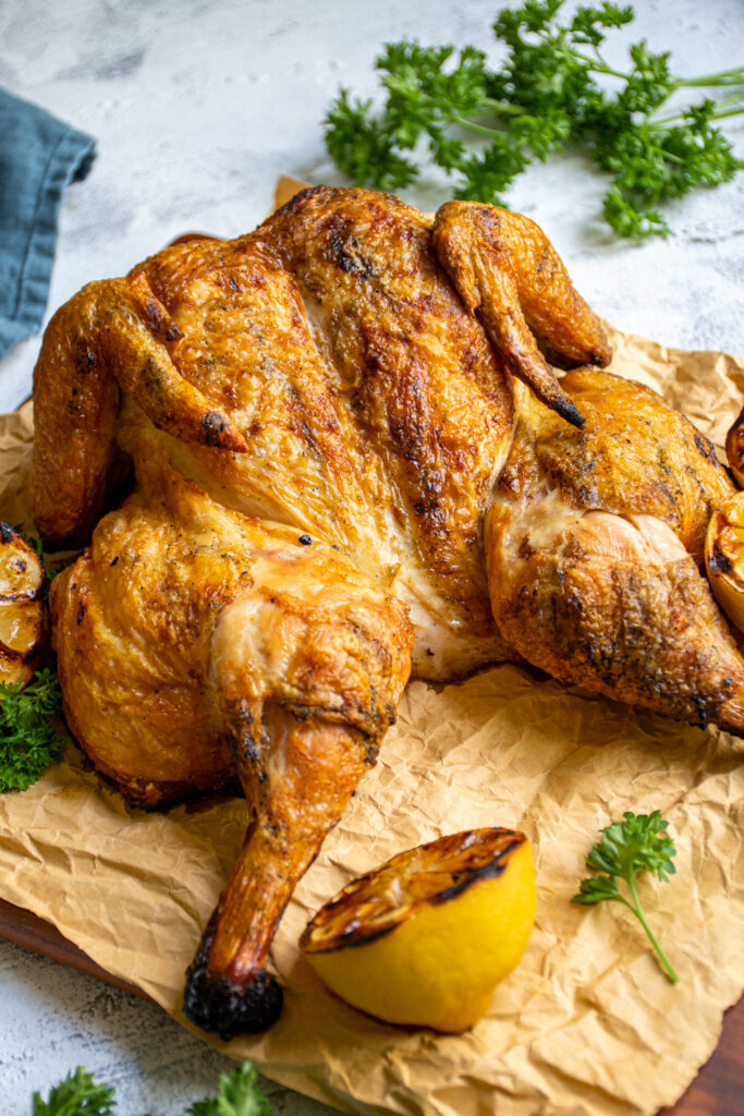 A Grilled Spatchcock Chicken grilled to golden perfection laid out on some brown butcher paper on top of a cutting board.