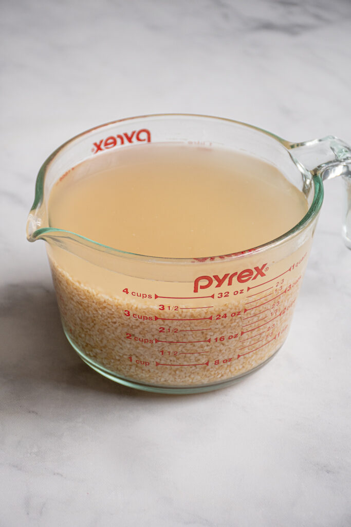 Large glass measuring cup filled with soaking bulgur and water.
