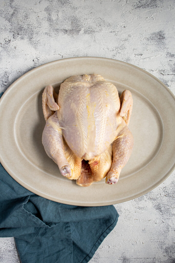A whole raw chicken sitting on a white platter.