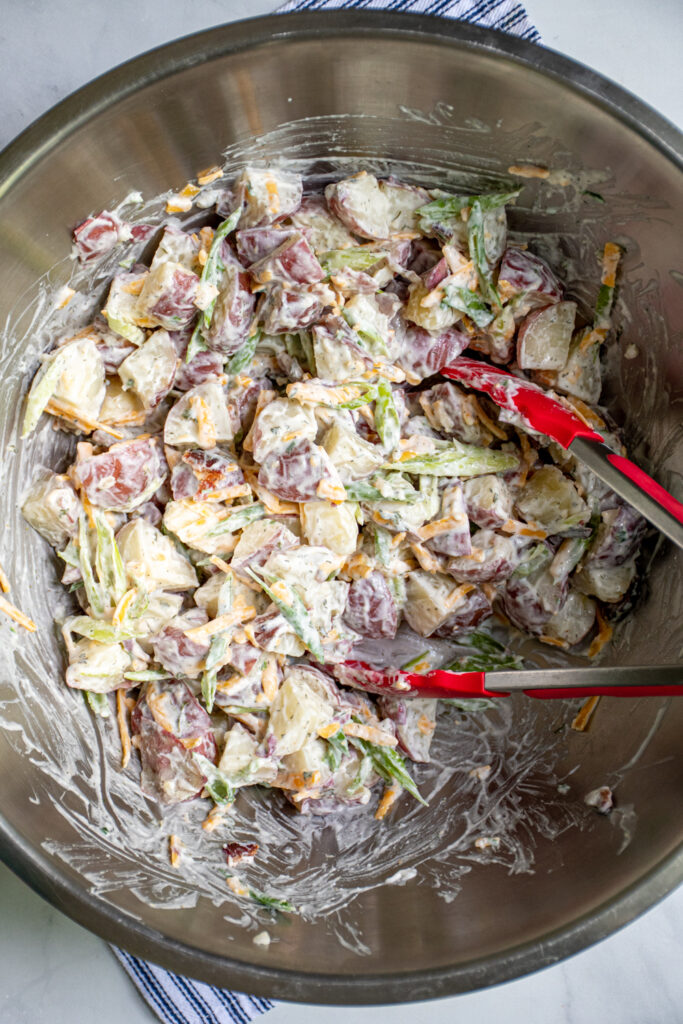 Overhead view of the freshly tossed bacon ranch potato salad in a large stainless steel bowl with a pair of tongs.