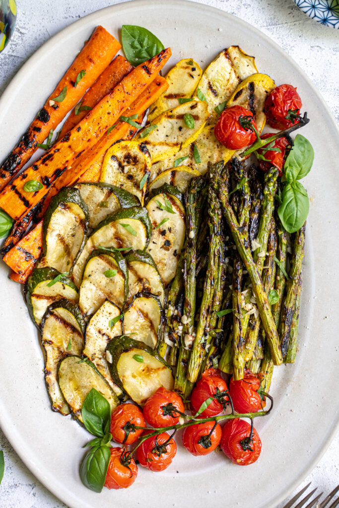 Close up of marinated grilled veggies on a platter covered in fresh basil.