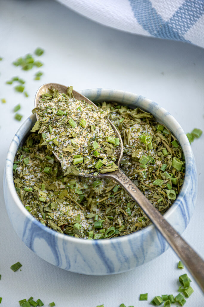Close up of a small blue and white bowl filled with ranch seasoning mix with a close of of a spoon that is filled with ranch seasoning.