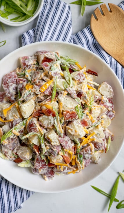A large white bowl filled with healthier bacon ranch potato salad filled with bacon bits, cheddar cheese, and sliced green onions.
