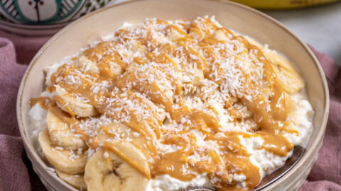White bowl gilled with cottage cheese and topped with banana slices, peanut butter, and shredded coconut.