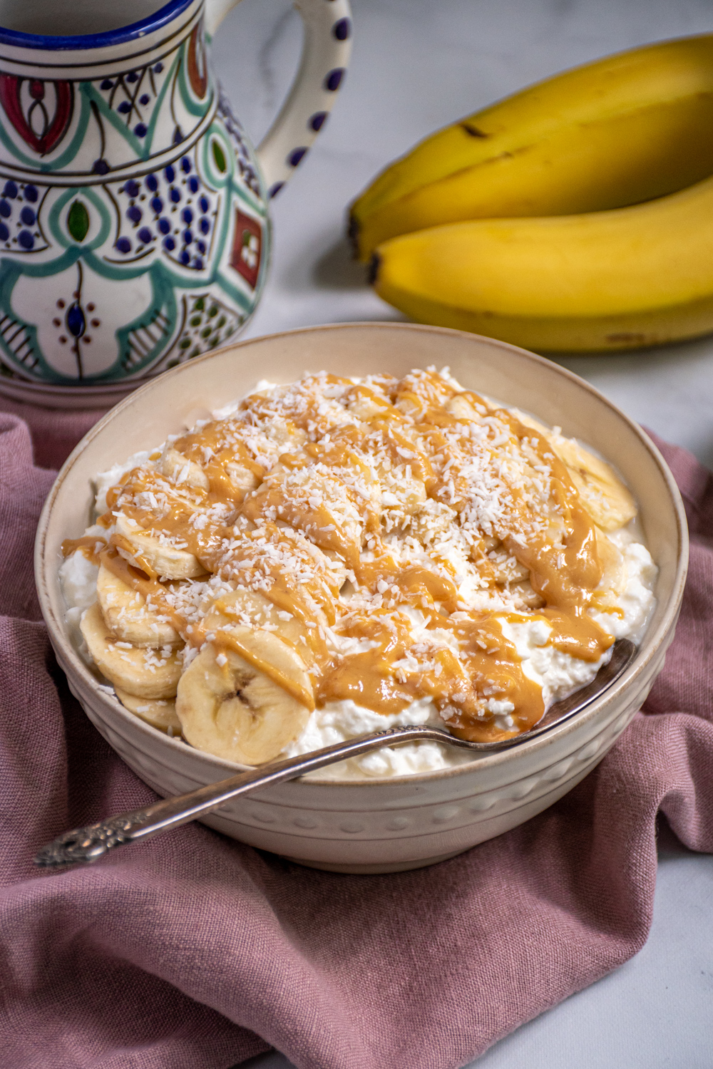 White bowl gilled with cottage cheese and topped with banana slices, peanut butter, and shredded coconut.