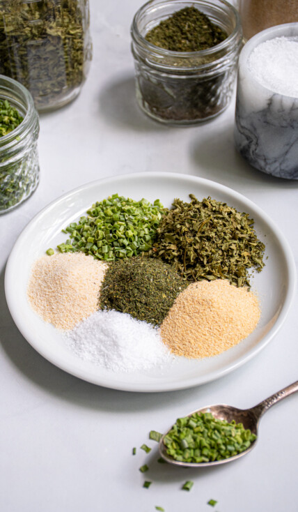 On a small white plate is little piles of 6 different spices that make up DIY Ranch Seasoning Mix.