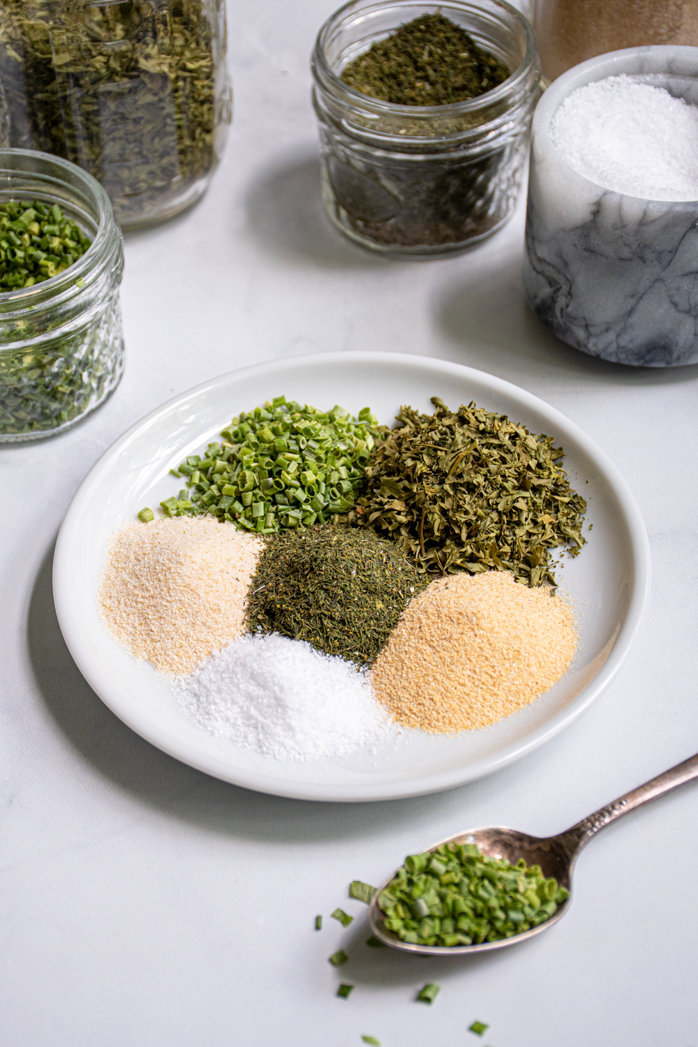 On a small white plate is little piles of 6 different spices that make up DIY Ranch Seasoning Mix.