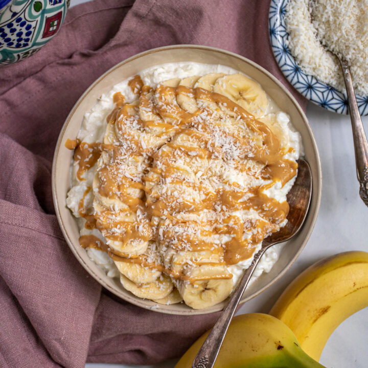 Overhead view of a bowl with a spoon filled with cottage cheese and topped with banana slices, drizzled peanut butter, and shredded coconut.