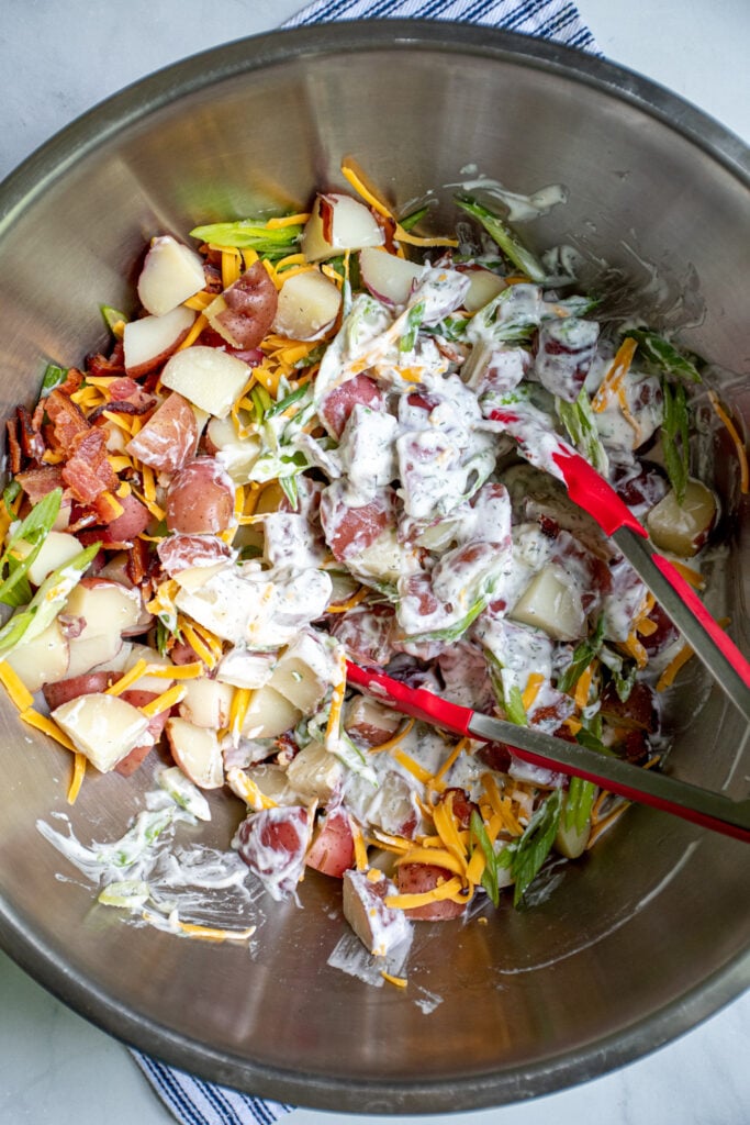 Tossing the bacon ranch potato salad in a large stainless steel bowl.