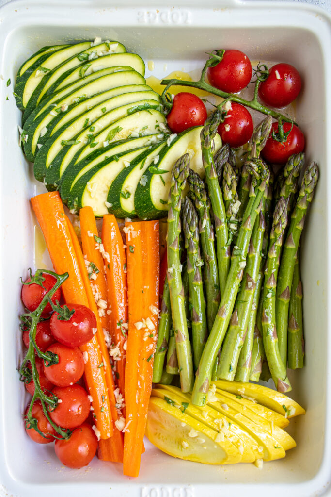 Raw and cut vegetables marinating in a baking dish before cooking.