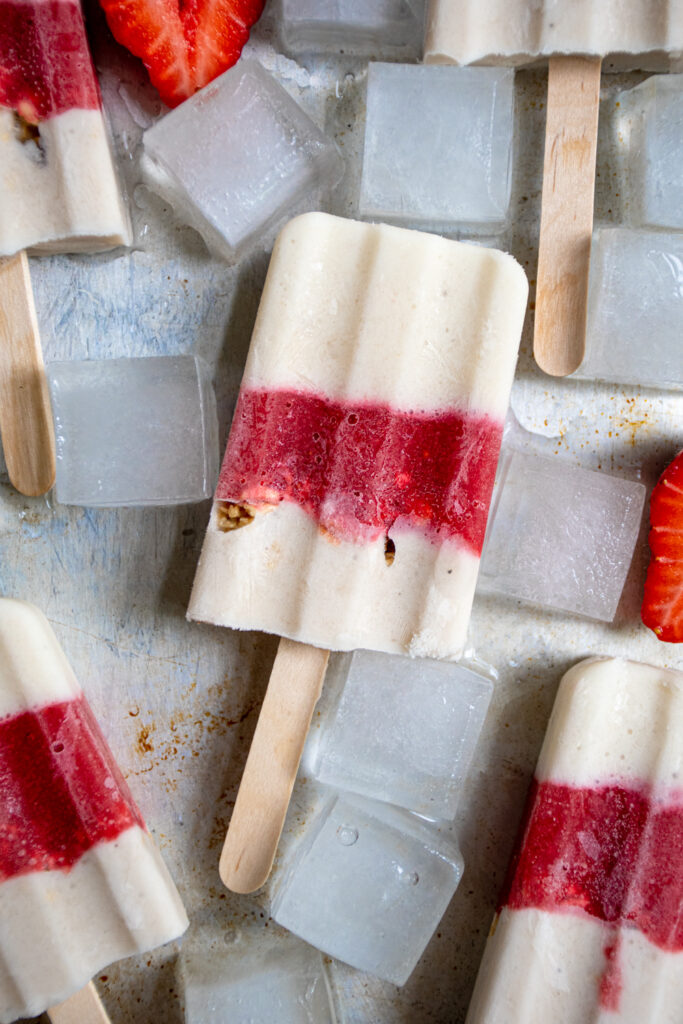 Close up of a red & white parfait popsicle on a sheet tray surrounded by ice cubes.