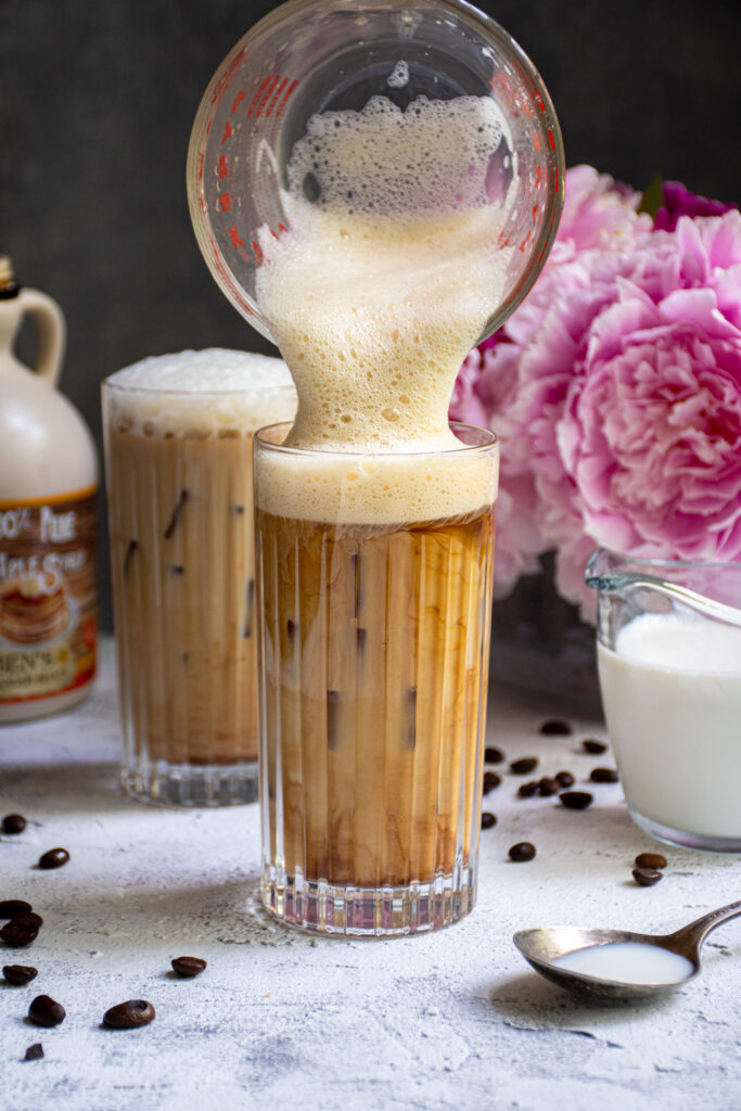 Salted Maple Foam being poured into a glass of cold brew coffee.