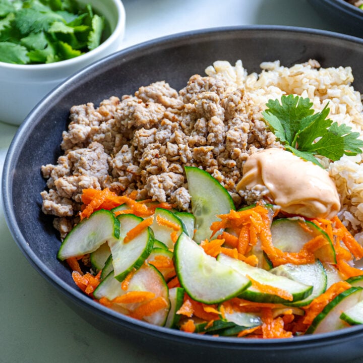 Close up of a bowl of brown rice, ground pork, and pickled vegetables topped with sriracha mayo.