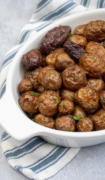Air fryer baby potatoes in a white ceramic serving dish covered in salt and garnished with chopped parsley.