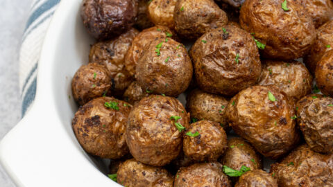 Air fryer baby potatoes in a white ceramic serving dish covered in salt and garnished with chopped parsley.