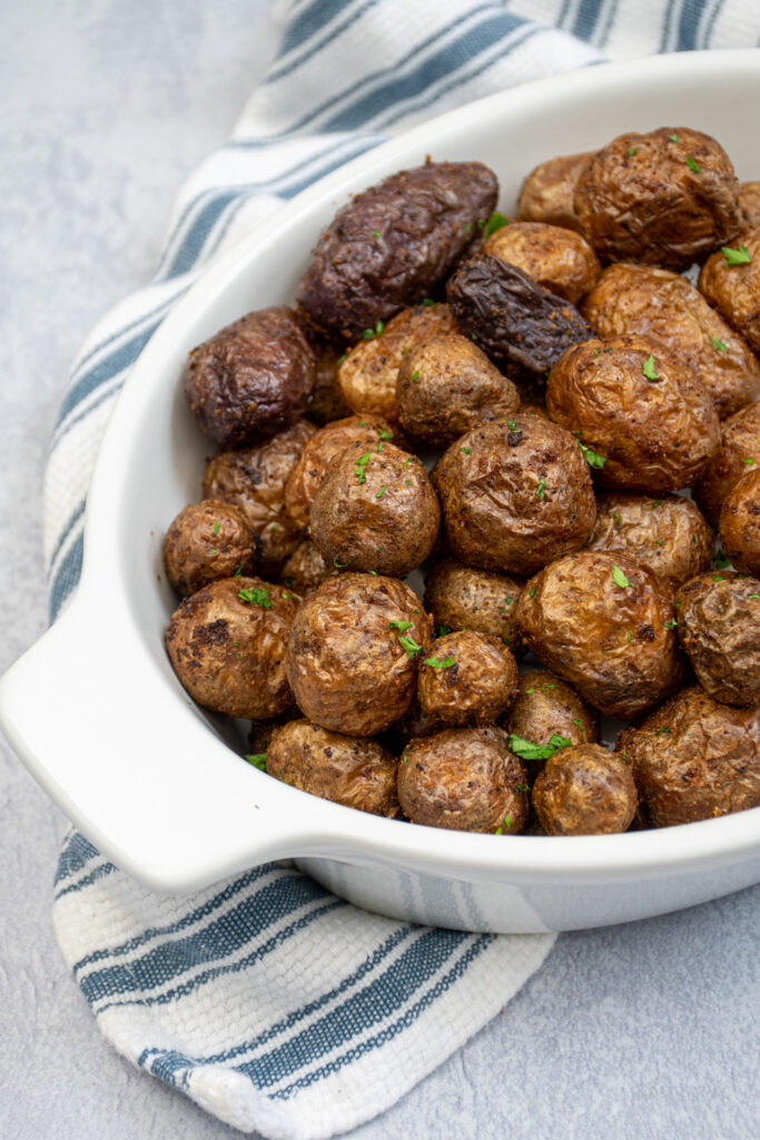 Air fryer baby potatoes in a white ceramic serving dish covered in salt and garnished with chopped parsley.