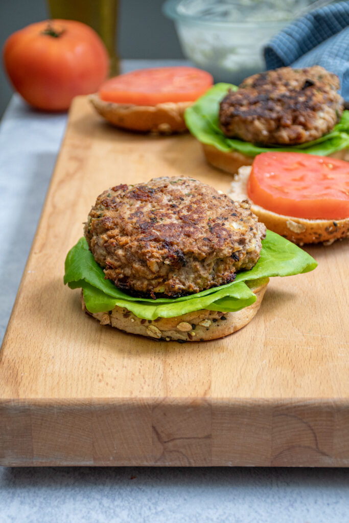 A greek turkey burger on a bun sit-in non a butcher block.