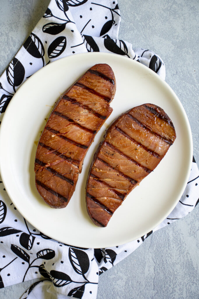 Grilled tuna steaks sitting on a white plate.
