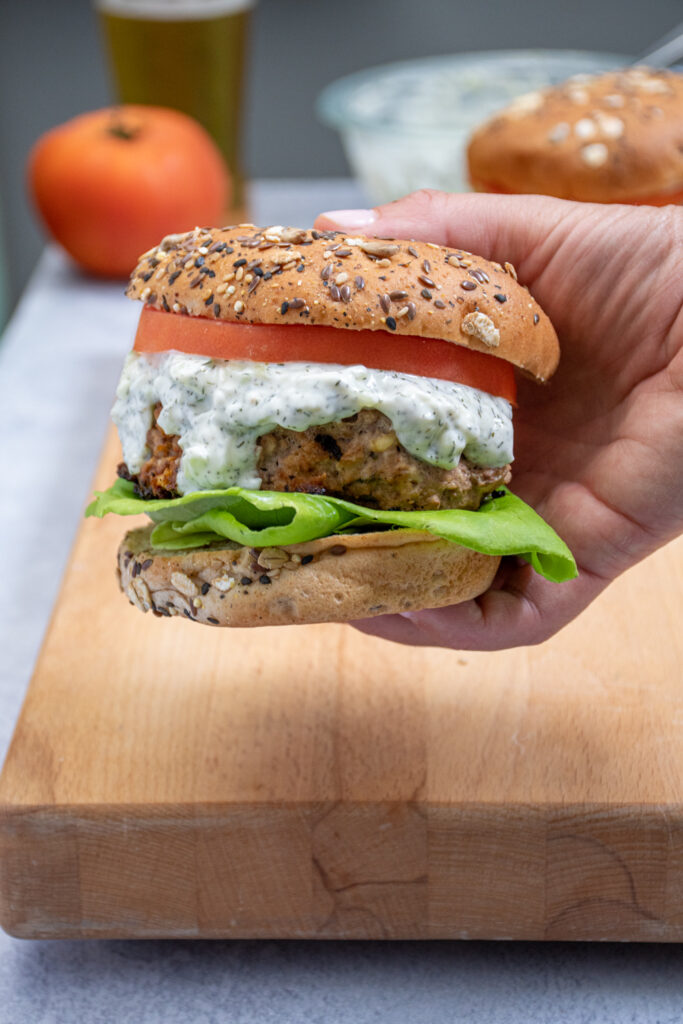 A hand holding up a Mediterranean Turkey burger with Tzatziki sauce dripping off the side.