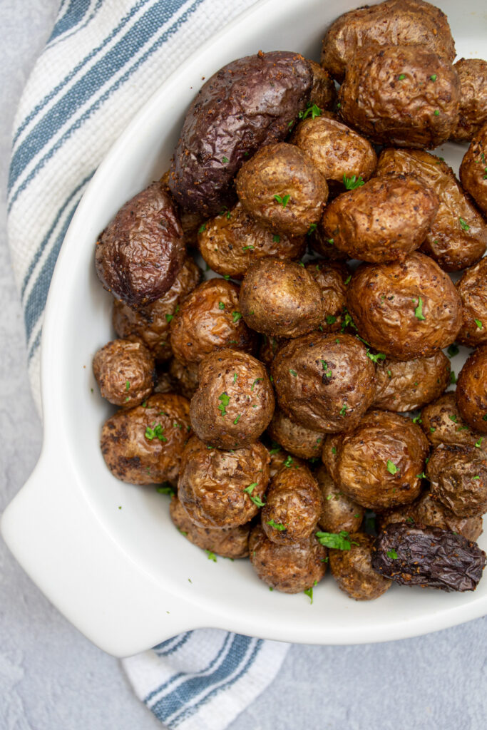 Overhead shot of a ceramic serving dish filled with crispy air fryer baby potatoes covered in salt and garnished with parsley.