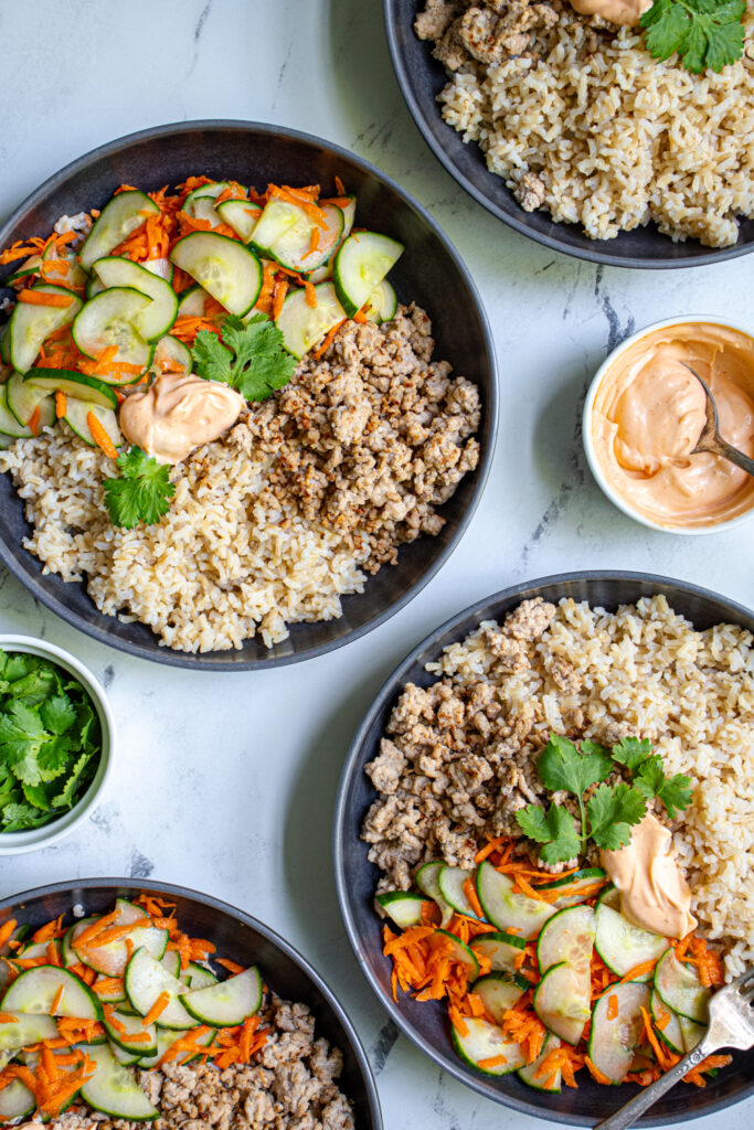 Photo of four bowls filled with brown rice, ground pork, and quick pickled vegetables.